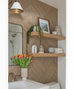 Powder room with a herringbone wood-look accent wall, floating oak shelves, an arched mirror and a brass faucet