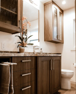 Remodeled bathroom in a Los Altos home with a walnut-toned vanity, glass-front wall cabinets and a veined stone countertop