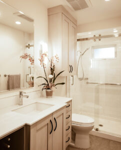 Bathroom with a light wood vanity, black arched pulls, tall wall cabinet and a glass sliding-door shower