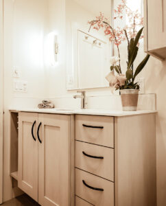 Light wood vanity with black curved handles, white countertop and a small open shelf at the end
