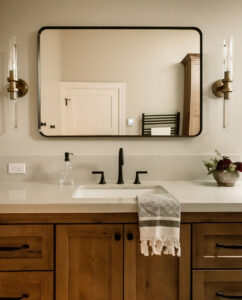 Bathroom vanity with rustic wood cabinet, black faucet, black-framed mirror and two glass wall sconces