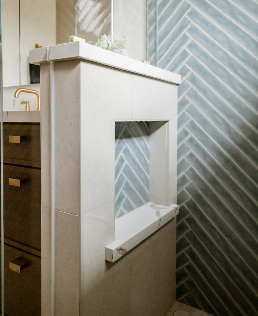 Shower half wall with a tiled niche and stone-look cap beside a dark wood vanity with gold pulls