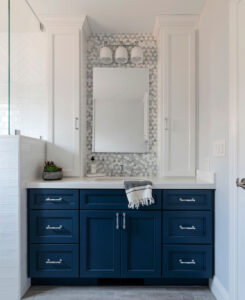Navy blue shaker-style vanity with silver pulls, flanked by tall white cabinets under a hexagon tile backsplash