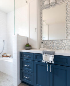 Navy vanity with a white countertop, hexagon mosaic backsplash and a short tiled wall beside the shower