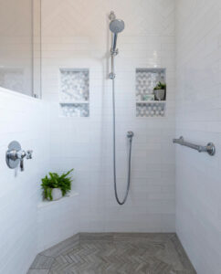 Walk-in shower with white subway tile, herringbone floor, two hexagon-tile niches and a handheld shower