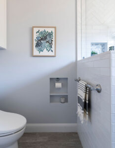 Bathroom wall with a recessed toilet paper niche, framed art and a subway-tile half wall by the shower