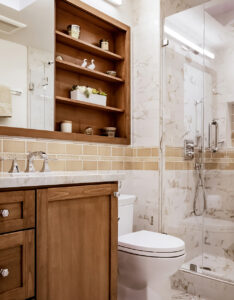 Bathroom vanity with a stained wood cabinet, recessed wall shelves and a tan tile border beside the glass shower