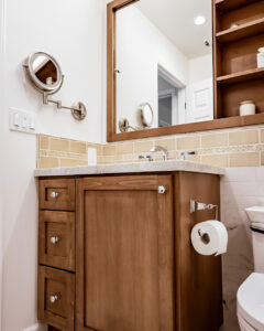 Wood vanity with drawer pulls, a framed mirror, a tan tile backsplash band and a swing-arm makeup mirror
