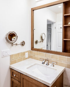 Undermount sink in a light stone-look countertop with a wood-framed mirror and tan tile backsplash