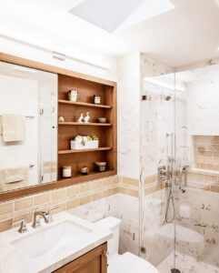 Small bathroom with a skylight, recessed wood shelves over the vanity and a glass-enclosed marble-look shower