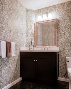 Powder room with leaf-pattern wallpaper, a dark vanity, a framed mirror and a dark stone-look floor