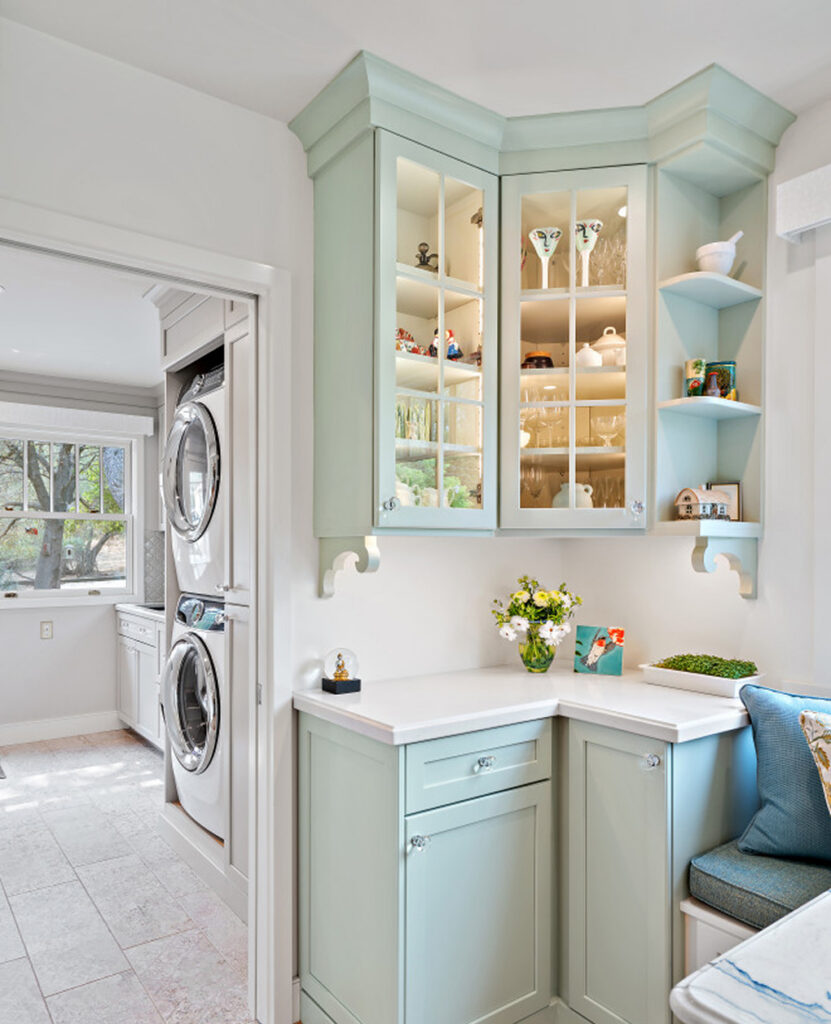 Corner glass-front cabinet in pale green with open shelves, and a view into the laundry room with stacked washer and dryer