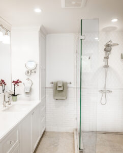 Bathroom with a white vanity, tall linen cabinet and a walk-in glass shower with a rain showerhead