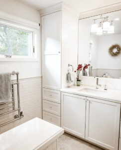 Vanity corner with a tall linen cabinet and drawers, and a chrome heated towel rack beneath a window