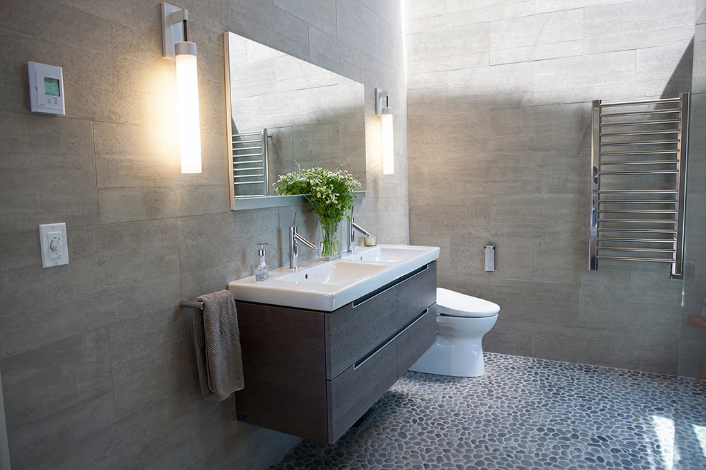 Remodeled primary bathroom with a floating double-sink vanity, gray stone-look wall tile and a pebble tile floor