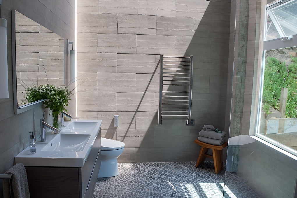 Primary bathroom with floating double vanity, heated towel rail, pebble floor and a window over a wood stool
