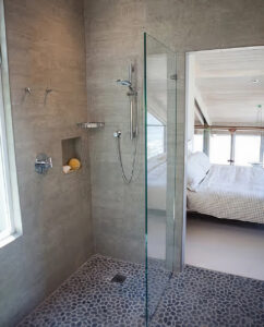 Walk-in shower with a frameless glass panel, handheld shower and tiled niche, with the bedroom visible beyond
