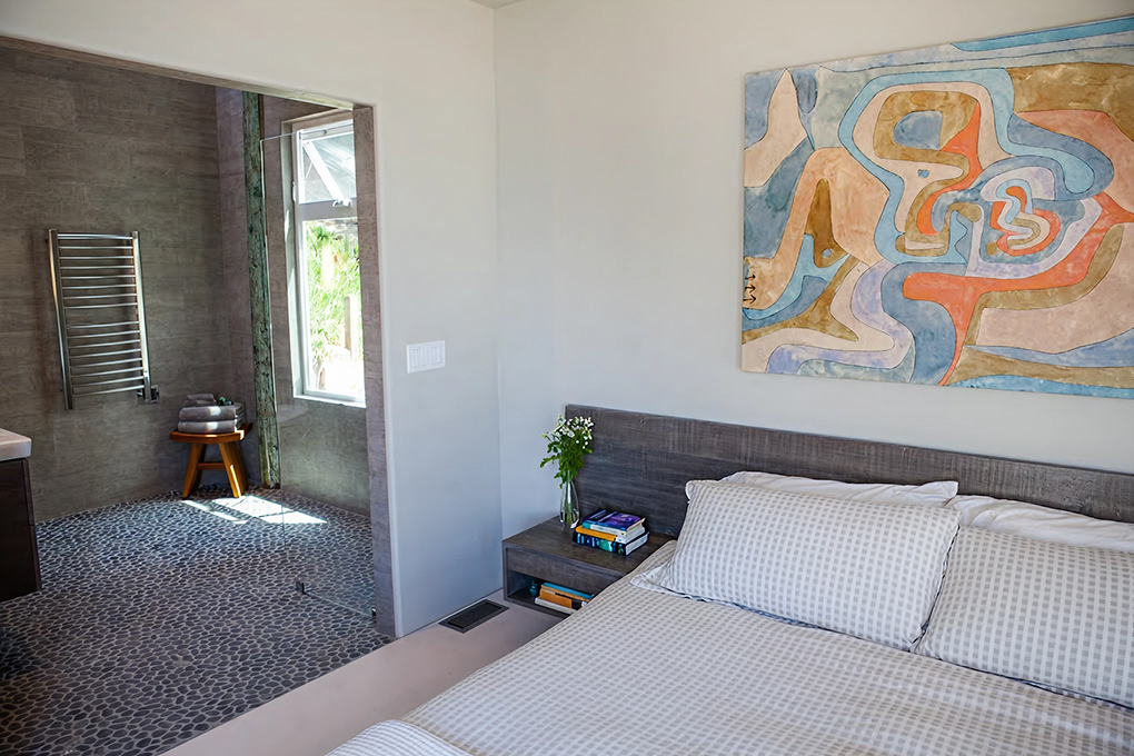 Bedroom with a plank-style headboard and abstract art, opening to the tiled primary bathroom